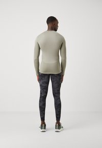 Fitted long-sleeve top in light green fabric, paired with black textured leggings featuring a subtle pattern. Athletic footwear completes the look.