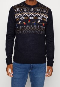 Granatowy sweter dzianinowy z motywami świątecznymi, w tym płatkami śniegu i żarówkami, z okrągłym dekoltem oraz ściągaczami przy mankietach i dolnej krawędzi.