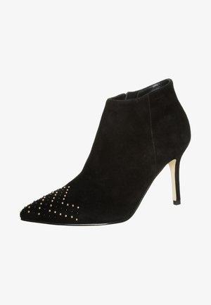 Botín de ante negro con punta afilada, que presenta acentos de tachuelas doradas y negras, y un tacón de aguja esbelto.