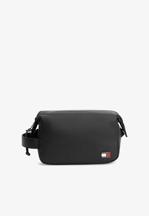 Musta suorakaiteen muotoinen toilettilaukku sivuhihnalla ja ylävetoketjulla, etuosan alaoikeassa kulmassa pieni Tommy Jeans -logotarra.