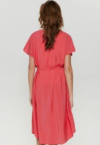 Rochie midi din coral cu mâneci scurte, talie strânsă și material fluid. Vedere din spate care arată textură netedă și cădere delicată.