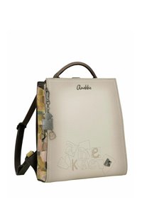 Sac à dos en cuir blanc avec une finition texturée, doté d'une poignée marron, d'un panneau latéral coloré et d'accents métalliques argentés. Détail de couture remarquable.