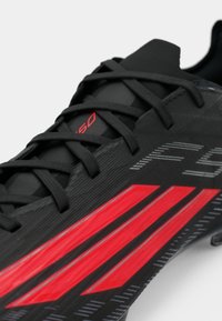 Μαύρα αθλητικά παπούτσια με κόκκινες λεπτομέρειες, με υφή, κομψό σχέδιο, εμφανή κορδόνια και λογότυπο στο πλάι.