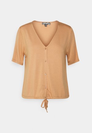 Short-sleeved, v-neck top in soft beige fabric, featuring a button front and adjustable tie detail at the hem. Smooth texture and relaxed fit.