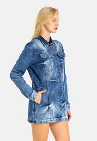 Denimjack in vervaagd blauw met een knoopsluiting aan de voorkant, twee borstzakken en zijzakken. Strak ontwerp met een klassieke kraag en lange mouwen.