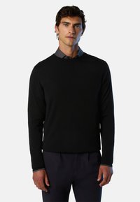 Pull en tricot noir à manches longues et col rond, porté par-dessus une chemise à col. Texture lisse avec une coupe décontractée.