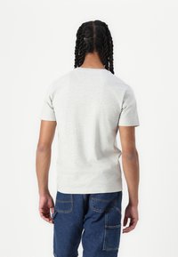 Lys grå kortærmet t-shirt i en figursyet design, med en rund halsudskæring og en glat tekstur. Båret med blå cargo bukser.