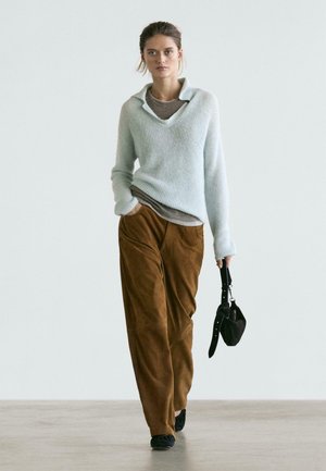 Maglione azzurro chiaro a coste con collo ampio, indossato sopra una maglietta grigia, abbinato a pantaloni larghi in suede marrone e una piccola borsa nera.