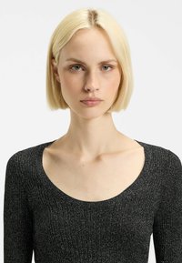 Top nero a coste con scollatura ampia, arricchito da fili metallici per un effetto scintillante e maniche lunghe. Tessuto liscio, design aderente.