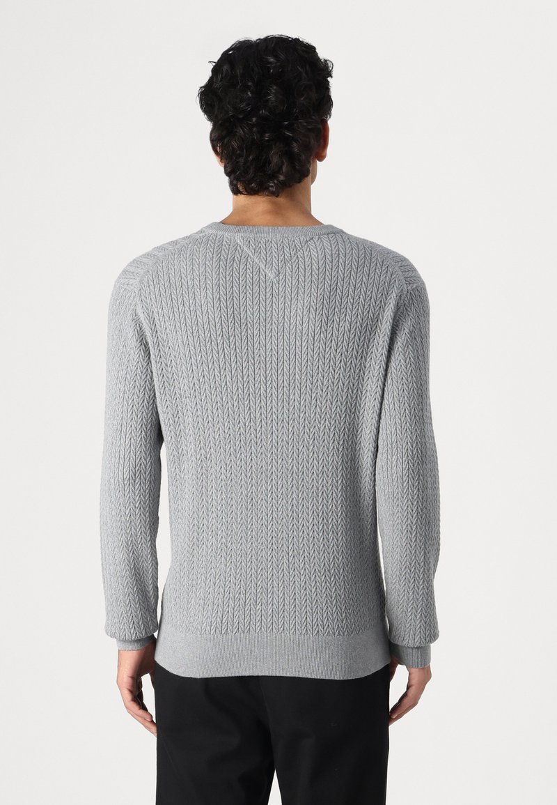 Pull en maille grise avec un motif chevron texturé. Présente des manches longues et un ourlet côtelé. La vue arrière montre un col en V et un tissu lisse.