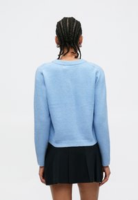 Vaaleansininen neulottu villapaita, jossa pitkät hihat, pyöreä pääntie ja resorireunus. Yhdistetty mustaan pliseerattuun hameeseen.