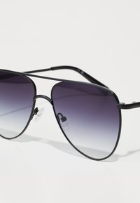 Sorte aviator solbriller med gradient fra mørk til lys lilla linser, metallramme og klare nesepads. Slank, minimalistisk design.