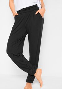 Pantaloni lounge neri con una fascia in vita ampia e tasche laterali, realizzati in un tessuto morbido ed elastico; presentano una vestibilità rilassata e gambe affusolate.