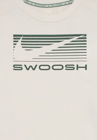 Bela tkanina z zelenim stiliziranim logotipom Nike swoosh nad besedo "SWOOSH" v krepkih zelenih črkah.