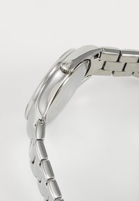 Relógio de aço inoxidável prateado com um acabamento polido, caixa redonda e um design de pulseira ligada. Apresenta uma coroa com acentos estriados.