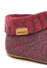 Rote und graue Filzschlappen mit einer weichen Textur, mit einem gerollten Rand und einem tanfarbenen Lederetikett, das "Gottstein" geprägt hat.