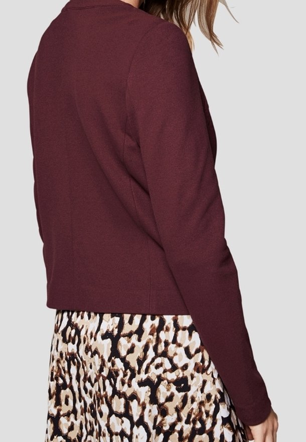 Femme portant une veste bordeaux à manches longues et une jupe avec un motif léopard beige et noir, vue de dos et de profil.