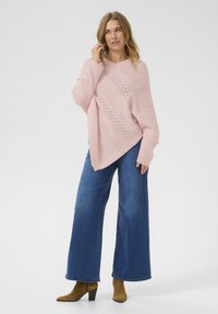 Světle růžový oversized svetřr se zigzag pleteným vzorem, kombinovaný s volnými modrými džíny a hnědými koženými kotníkovými botami na podpatku.