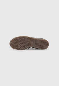 Brown rubber shoe sole with a textured surface and circular patterns. Features a triangular tread design and an embossed logo.