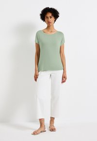 Lichtgroen kort mouwen top gecombineerd met witte wijde pijpen broek en huidskleurige sandalen met bandjes, met een relaxte pasvorm en een gladde textuur.