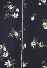 Tissu bleu marine avec une fermeture éclair argentée au centre et un motif dispersé de fleurs blanches avec des feuilles vertes.