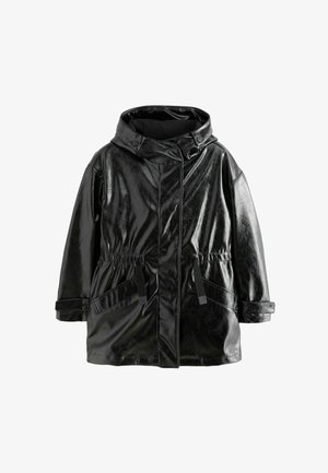 Schwarze, glänzende, wasserdichte Parka mit verstellbarem Bund, Kapuze und großen Taschen, kombiniert mit grauen Jeans und schwarzen klobigen Stiefeln.
