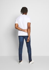 Camiseta blanca de manga corta, combinada con vaqueros azul oscuro. Diseño minimalista, textura suave. Calzado: zapatillas blancas con detalles en negro.