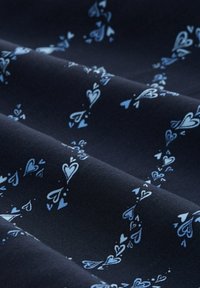 Tissu bleu marine à texture lisse, avec un motif dispersé de cœurs bleu clair créant un design distinct.