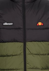 Schwarze und grüne Steppjacke mit einem frontalen Reißverschluss. Verfügt über ein gesticktes Logo und ein Muster aus gesteppten Abschnitten. Strukturiertes Material.