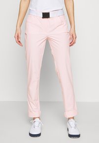 Ljusrosa byxor med en mjuk textur, med en rullad fåll och fyra fickor. Kombineras med vita skor och ett bälte.