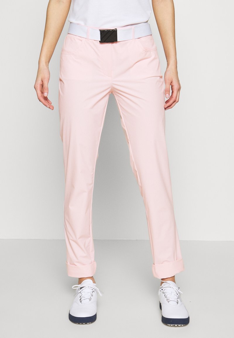 Světle růžové kalhoty s hladkou texturou, s ohrnutým lemem a čtyřmi kapsami. V kombinaci s bílými botami a opaskem.