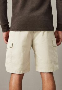 Beige cargo rövidnadrág oldalsó zsebekkel, könnyű anyagból készült. A design géppel varrott részletekkel és laza szabással rendelkezik.