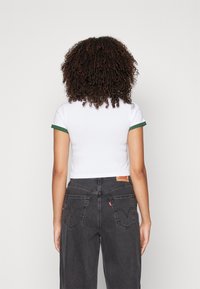 Valkoinen lyhyt t-paita, jossa vihreät resorimitat hihansuissa, yhdistetty korkeavyötäröisiin mustiin farkkuihin, joissa on kirjotut takataskut ja merkin logo.