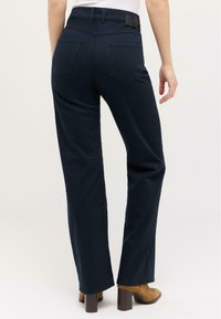 Dark blue high-waisted jeans with back pockets and a straight-leg design, paired with tan heeled boots. Smooth fabric texture.