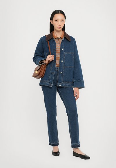 Jeans jakna z rjavim kordiranim ovratnikom, dvema sprednjima žepoma, kombinirana s črtasto srajco in jeans hlačami, dopolnjena s črnimi ravnimi čevlji.