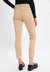 Beige ribfluwelen broek met een slim fit, voorzien van achterzakken en een gladde textuur. Het enkel-lange ontwerp wordt gecombineerd met zwarte platform schoenen.