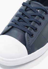 Mörkblå sneakers med en slät läderöverdel, texturerade mörkblå snören, vit gummikappa vid tån och en minimalistisk design med tonalt sömnad.
