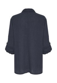 Camicia blu scuro in tessuto leggero, con colletto a piega e maniche arrotolate. La finitura testurizzata aggiunge interesse visivo.
