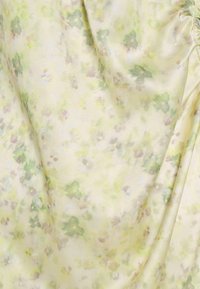 Kwiatowa tkanina charakteryzuje się miękką, jedwabistą teksturą w jasnym żółtym kolorze z zielonymi liśćmi i drobnymi kwiatami, tworząc subtelny, zblendowany wzór.