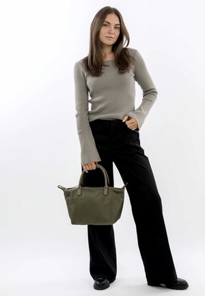 Borsa a tracolla verde oliva con forma strutturata, doppi manici superiori e chiusura a zip, abbinata a un maglione beige a coste e pantaloni neri a zampa.