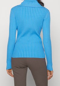 Niebieski prążkowany sweter z golfem z długimi rękawami i fakturowaną tkaniną, dopasowany krój podkreślający kształt ciała, w zestawieniu z brązowymi spodniami.