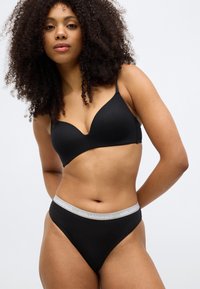 Čierna bezšvová podprsenka s výstrihom do tvaru písmena V a nastaviteľnými ramienkami, v kombinácii s čiernymi vysokými nohavičkami s sivým pásikom so značkou.