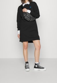 Vestido sudadera negro, con cuello blanco, bolso cruzado negro con diseño estampado y zapatillas altas negras con suela blanca.