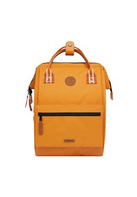 Oranje canvas rugzak met bruine leren accenten, dubbele handgrepen aan de bovenkant, voorste ritszak en een ronde logopatch. Gekartelde onderkant.