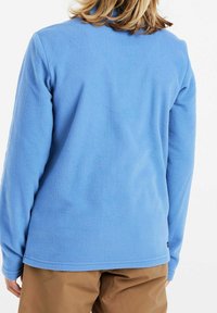 Jasnoniebieska polarowa kurtka o miękkiej fakturze, z długimi rękawami i okrągłym dekoltem, zestawiona z beżowymi spodniami, tworząc swobodny wygląd.