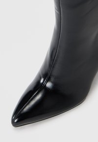 Stivaletto in pelle nera a punta, con texture liscia, design elegante e dettagli di cucitura visibili lungo la cucitura.