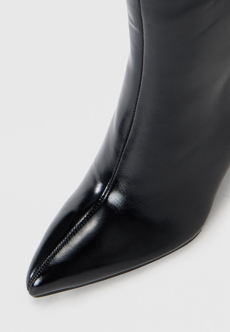 Zwarte leren enkelboot met een puntige neus, gladde textuur, slank ontwerp en zichtbare stiksels langs de naad.
