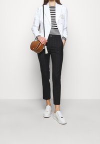 White blazer with a crest, black and white striped shirt, pinstripe trousers, and white sneakers, complemented by a brown crossbody bag.