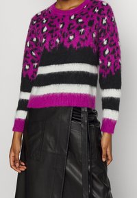 Fuzzy pink and black sweater featuring a leopard print design, black stripes, and white accents. The sweater has long sleeves and a crew neckline.