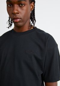 T-shirt en coton noir avec un col rond et des manches courtes, orné d'un logo brodé discret sur la poitrine. Texture douce, coupe décontractée.